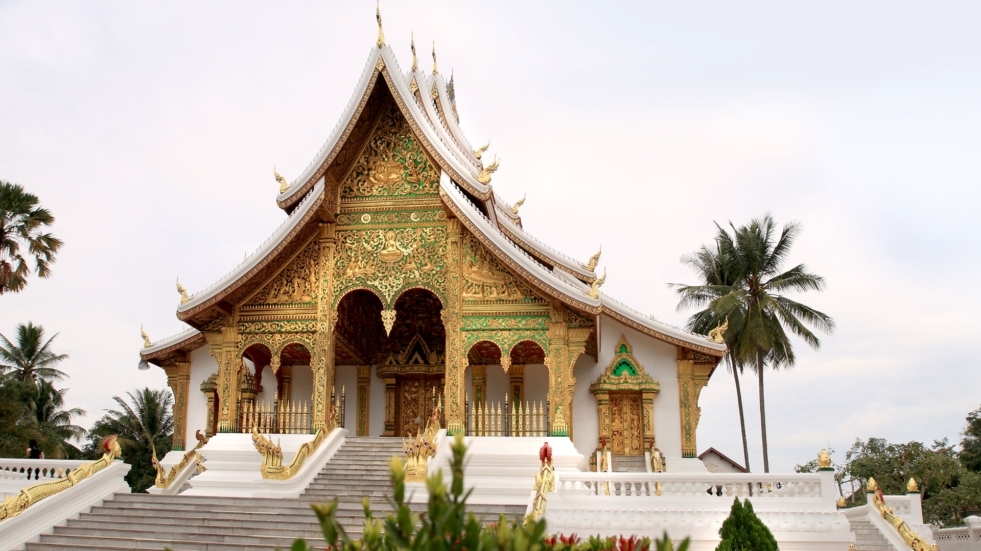Ornate gilded Buddhist temple with sweeping tiered roofs and palms